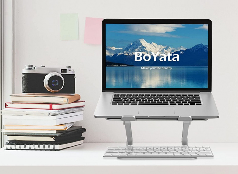   En Boyata bärbar dator står på ett skrivbord bredvid en staplad hög med böcker med en kamera ovanpå