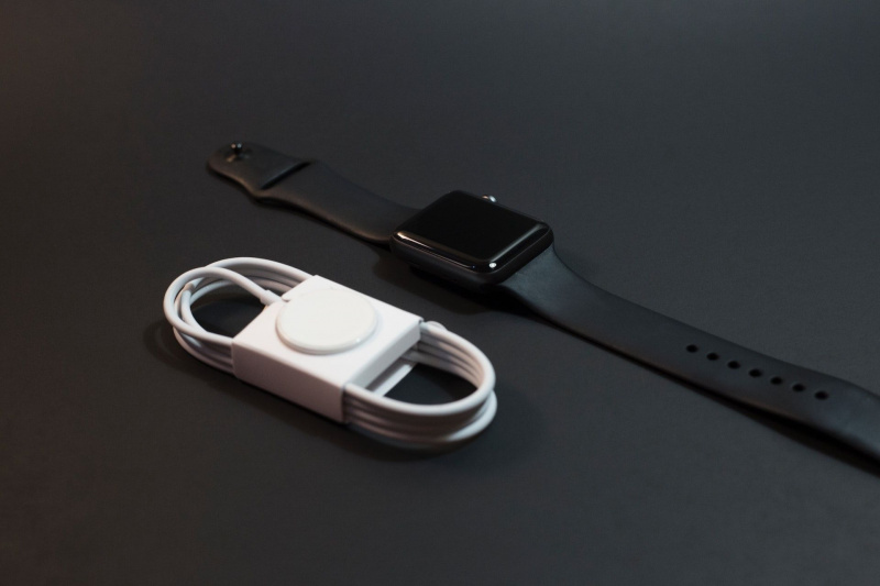   Apple Watch بسوار أسود بجانب شاحن Apple Watch جديد