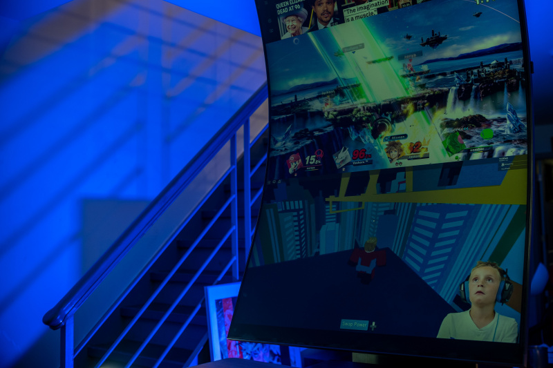   Samsung Odyssey Ark 55in în modul Cockpit afișând un program TV în partea de jos, iar Super Smash Bros în mijlocul ecranului, cu aplicația Youtube pe ecranul de sus