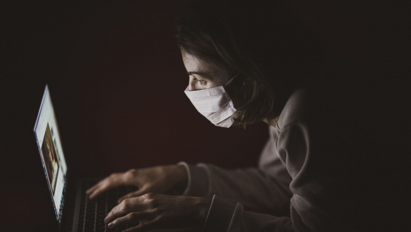   femeie pe laptop care poartă mască de față