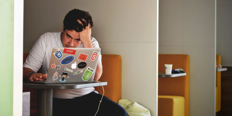   Стресиран мъж, използващ MacBook, държейки главата си